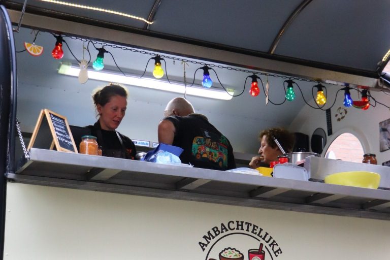 Drie mensen werken in een foodtruck met kleurrijke verlichting.