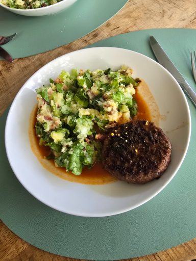 Een bord met een groentesalade en een plakje hamburger op een groene placemat.